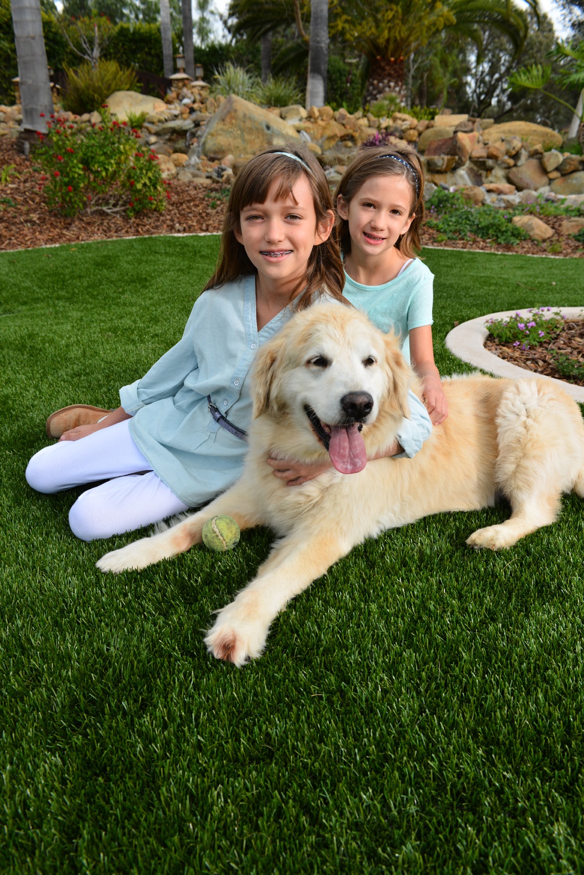 Girls sitting on turf next to their dog